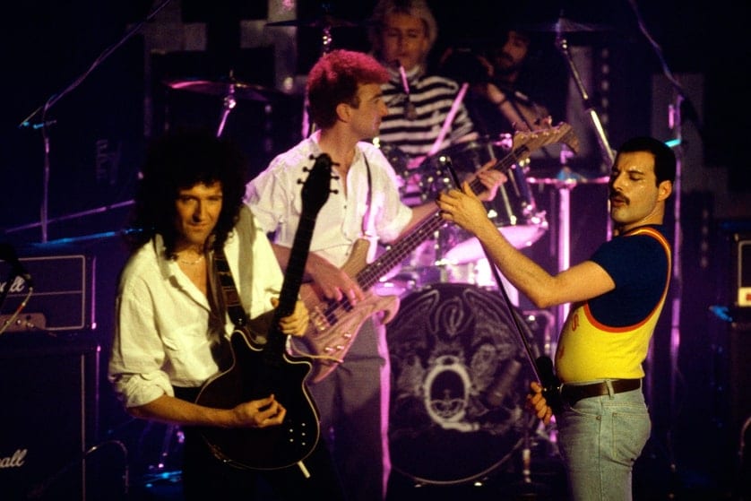 Queen au grand complet sur la scène de la Rose d’Or : Brian May, John Deacon, Roger Taylor et Freddie Mercury, devant le blason du groupe.