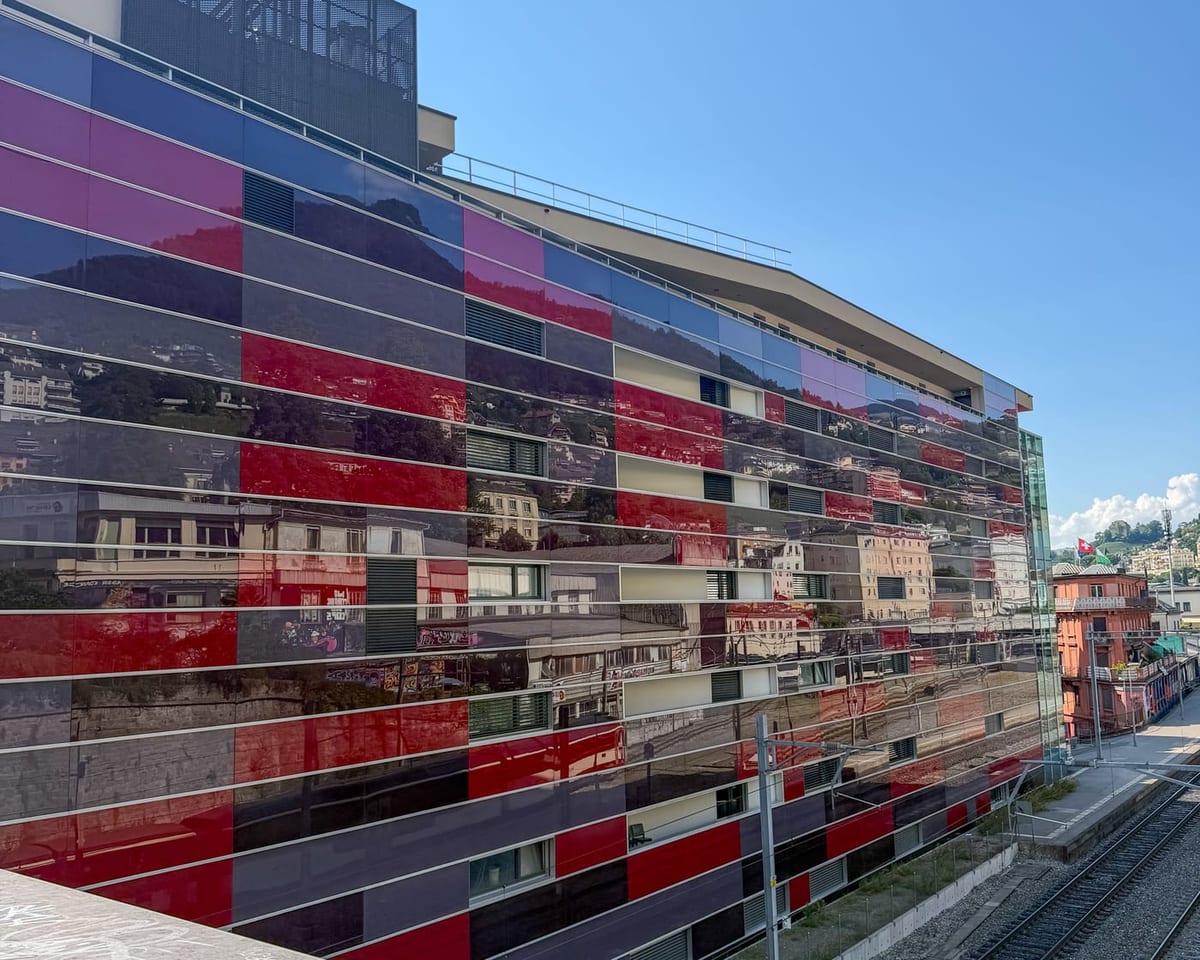 La façade de verre coloré du Freddie Mercury Hotel, ornée de vues de l’ancien Montreux, le long des voies.